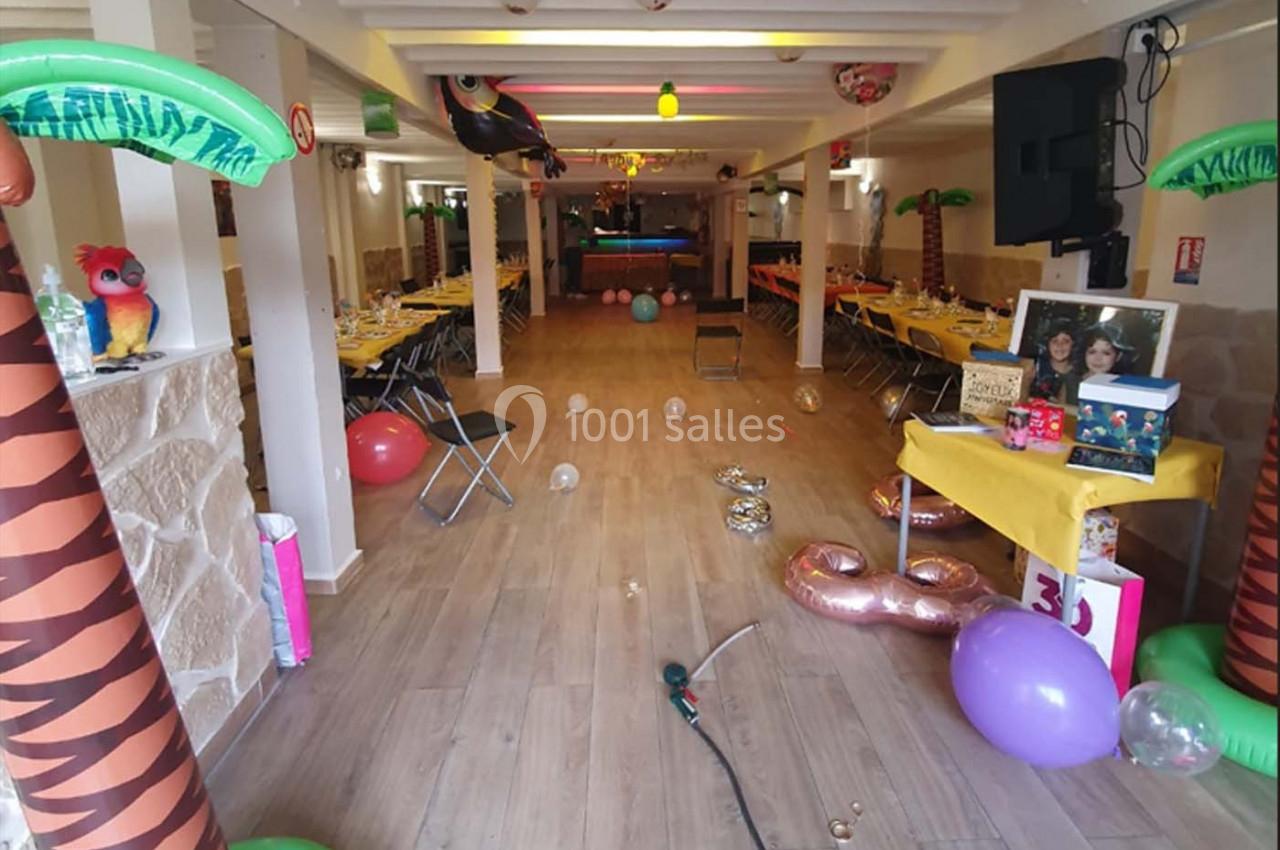 Salle décorée sur le thème tropical avec tables dressées, ballons colorés et palmiers gonflables.