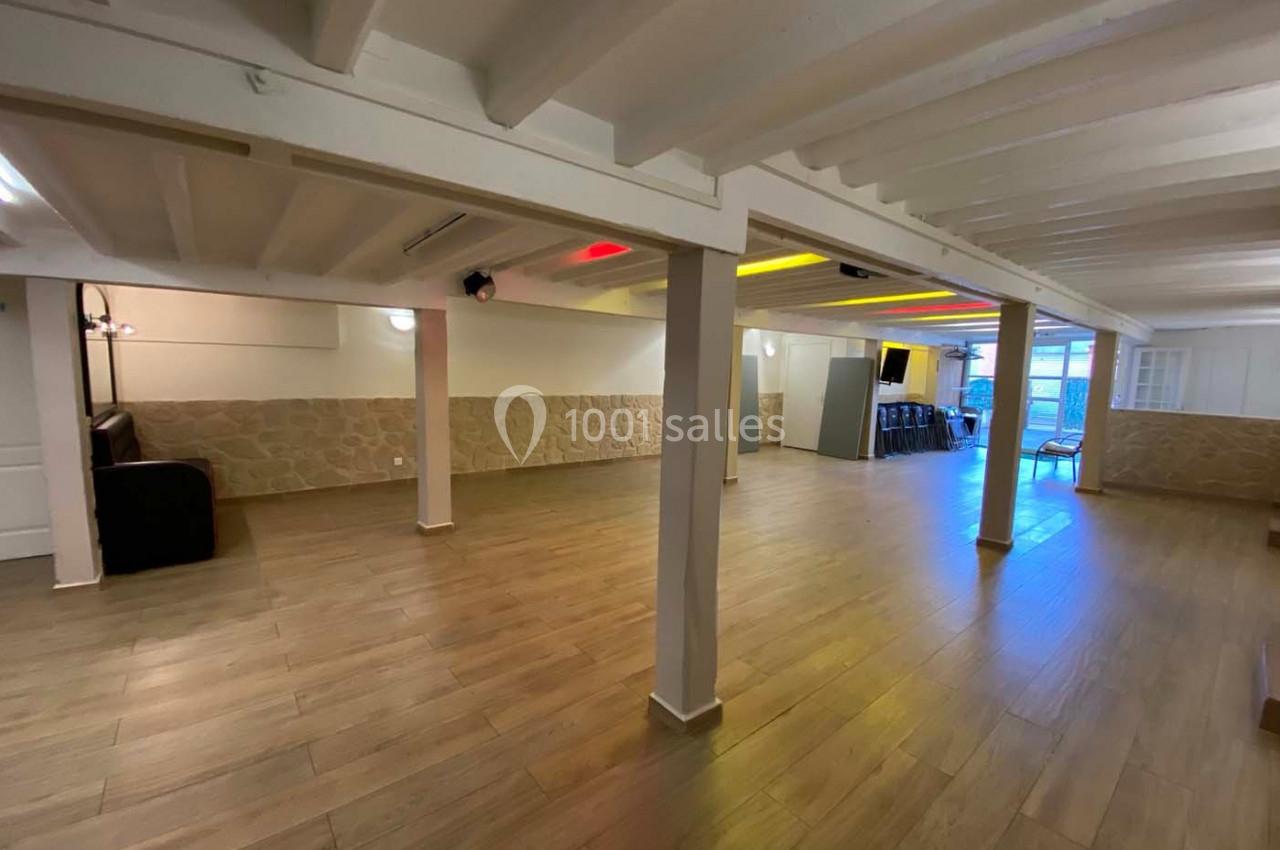 Salle spacieuse avec parquet, murs en pierre et poutres apparentes, éclairée par des lumières colorées.