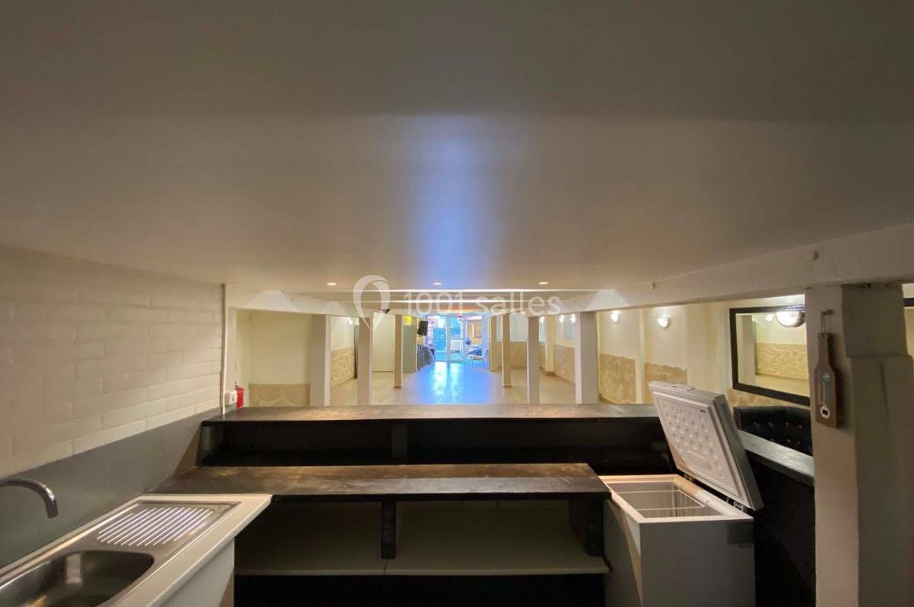 Vue d'un espace intérieur avec un comptoir, un évier, un congélateur ouvert et un couloir éclairé en arrière-plan.