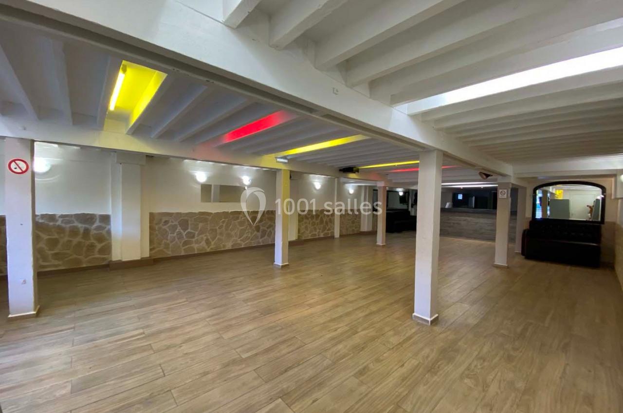 Salle vide avec sol en parquet, murs en pierre et plafond blanc avec éclairage coloré intégré.