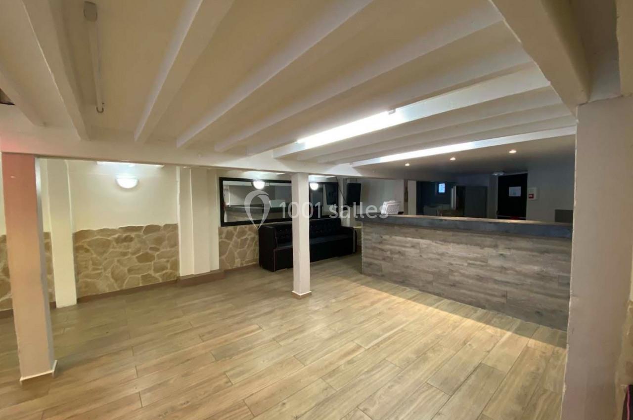 Salle vide avec sol en parquet, murs en pierre et crépi, poutres apparentes au plafond, et comptoir en bois.