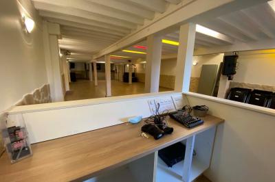 Salle spacieuse avec sol en parquet, murs en pierre et poutres blanches apparentes, éclairée par des lumières modernes.