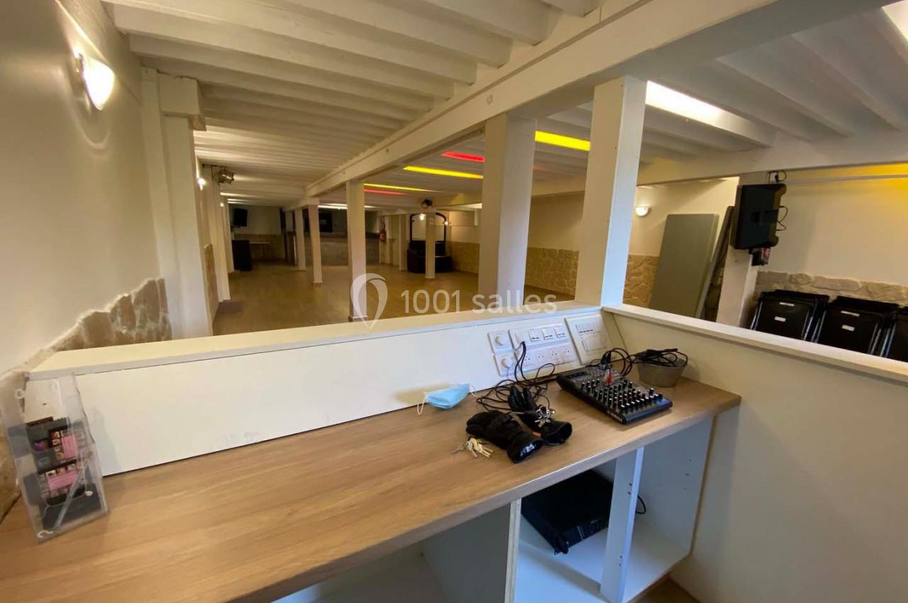 Vue d'une salle polyvalente avec un plafond en poutres apparentes, un bureau équipé de matériel audio au premier plan.