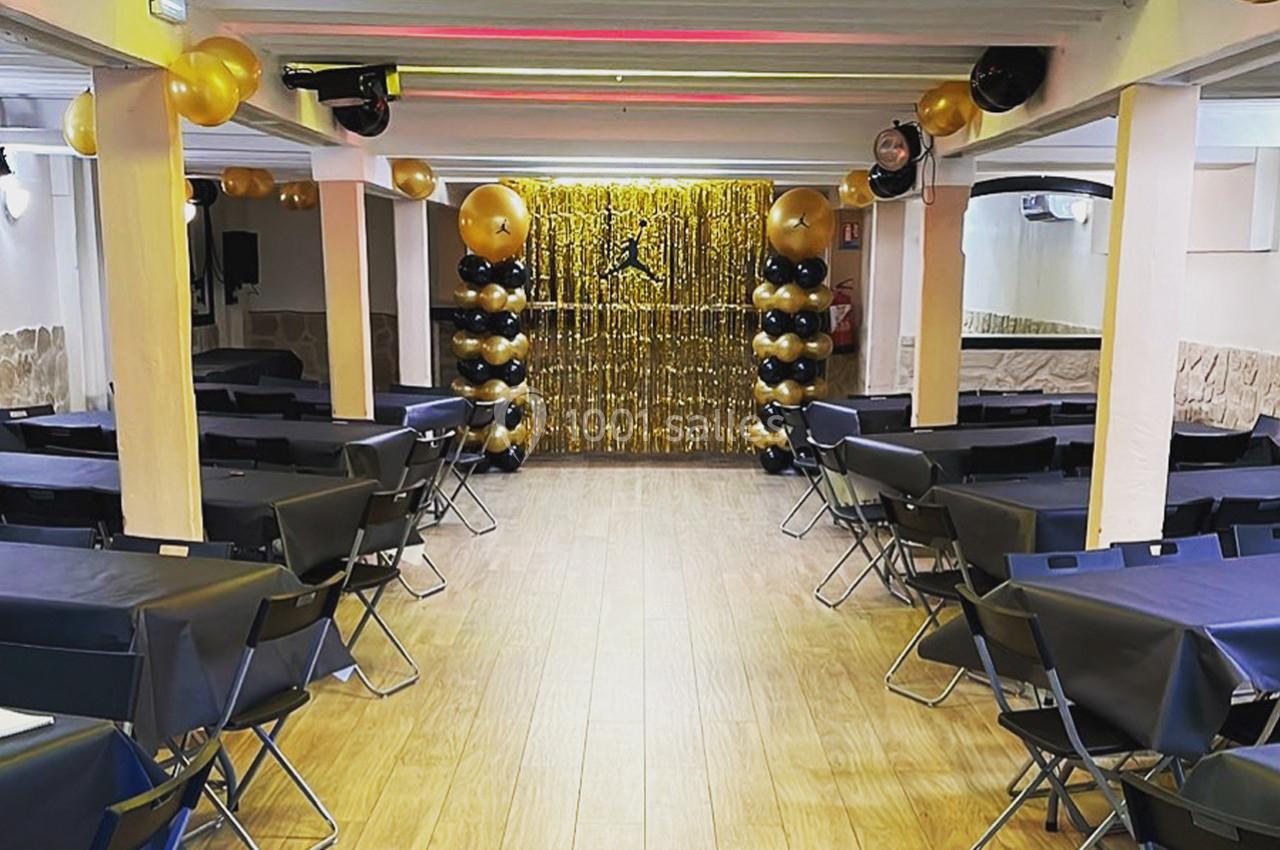 Salle décorée pour un événement avec des tables noires, des ballons dorés et noirs, et un fond scintillant doré.