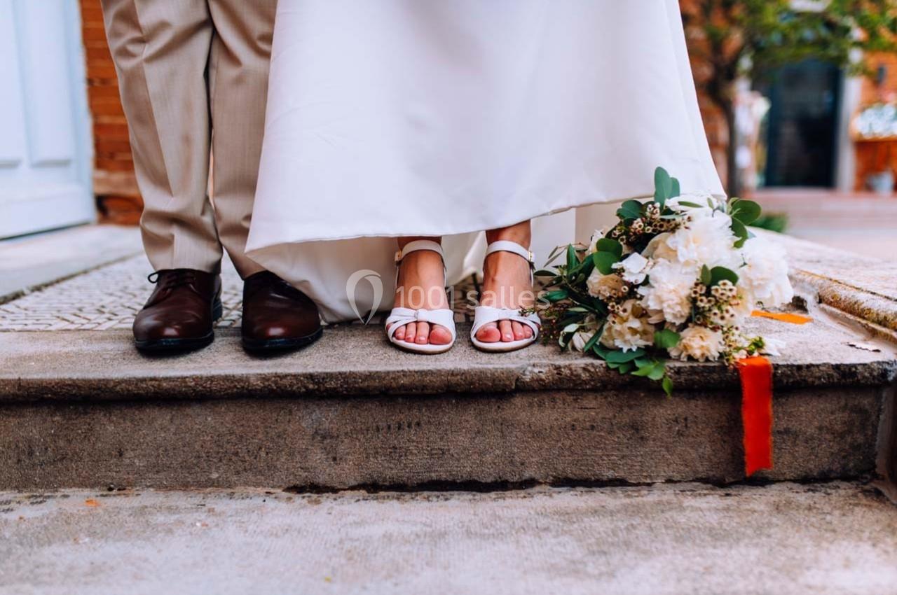 Les pieds d'un couple en tenue de mariage, avec un bouquet de fleurs posé sur le sol à côté d'eux.