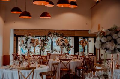 Salle de réception avec tables rondes dressées, décorées de fleurs, bougies et couverts élégants.