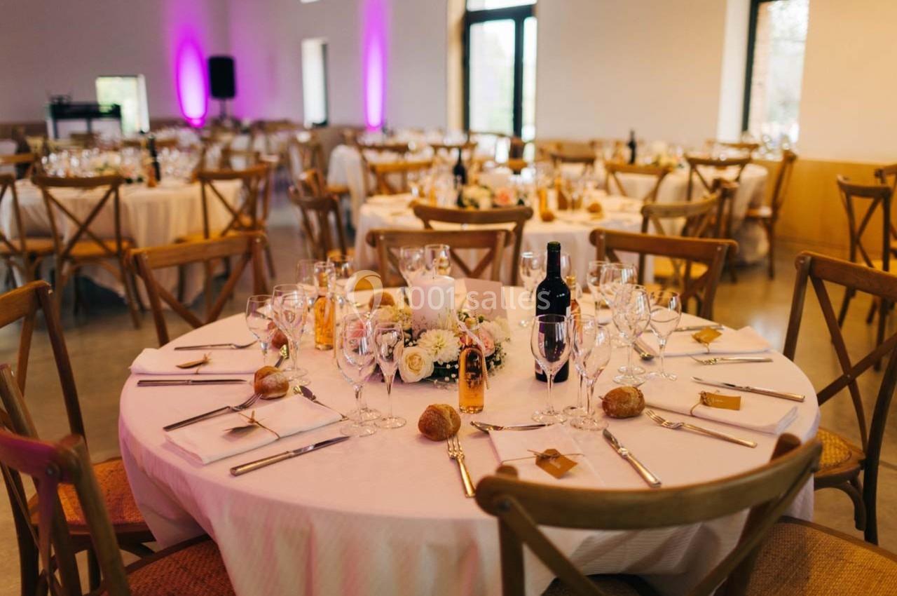 Salle de réception avec tables rondes dressées, décorées de fleurs, bougies et couverts élégants.