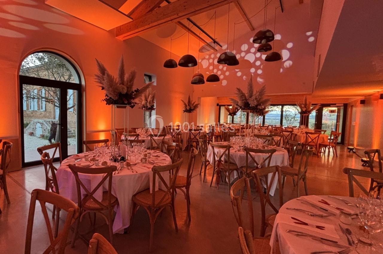 Salle de réception décorée avec des tables rondes, des chaises en bois et un éclairage tamisé aux tons chauds.
