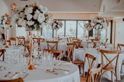 Salle de réception avec tables rondes dressées, décorées de fleurs, bougies et couverts élégants.