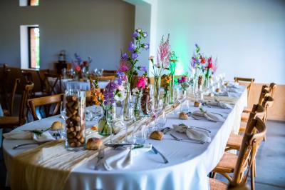 Salle de réception avec tables rondes dressées, décorées de fleurs, bougies et couverts élégants.