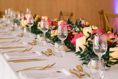 Salle de réception avec tables rondes dressées, décorées de fleurs, bougies et couverts élégants.