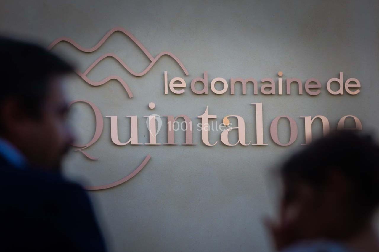Enseigne murale indiquant ’Le Domaine de Quintalone’ avec des silhouettes floues au premier plan.