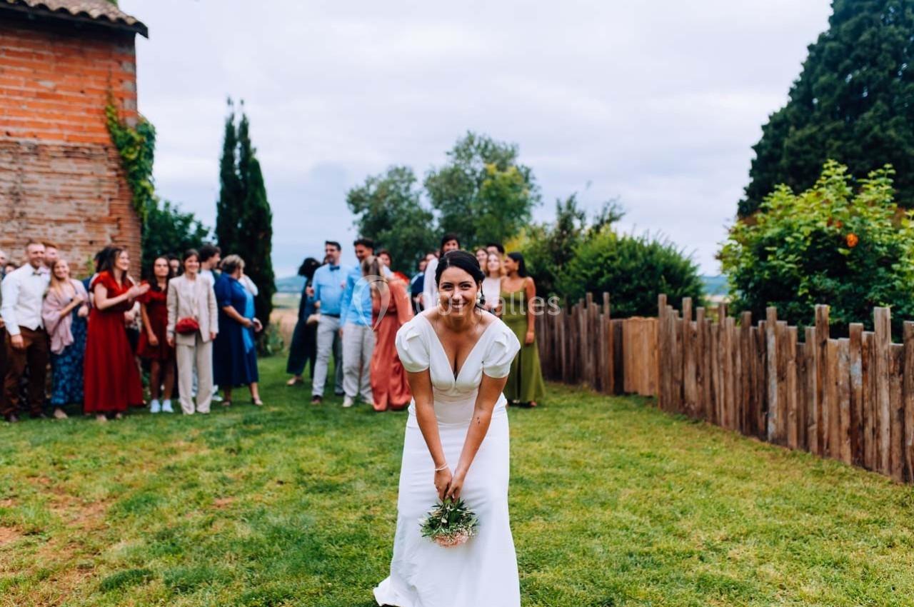 Une mariée souriante s'apprête à lancer son bouquet, entourée d'invités dans un jardin.