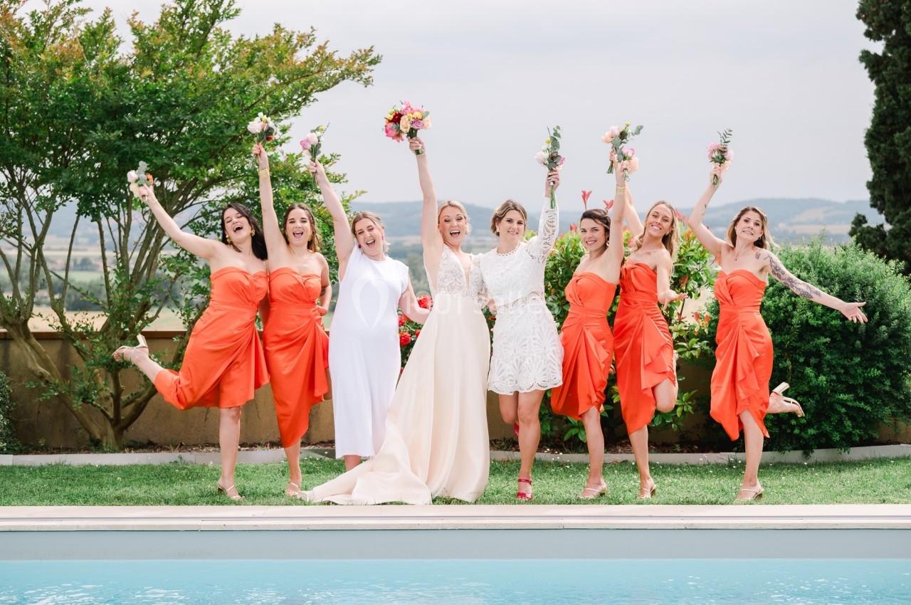 Un groupe de femmes en robes colorées pose joyeusement près d'une piscine, certaines tenant des bouquets.