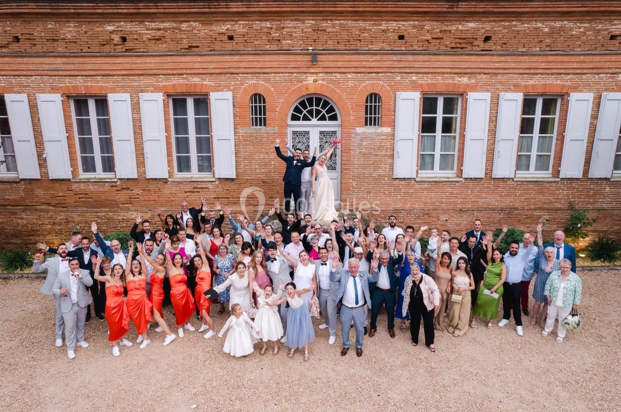 Groupe de personnes rassemblées devant un bâtiment en briques, célébrant un mariage avec des tenues festives.