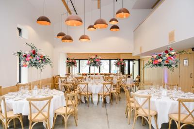 Salle de réception avec tables rondes dressées, décorées de fleurs, bougies et couverts élégants.