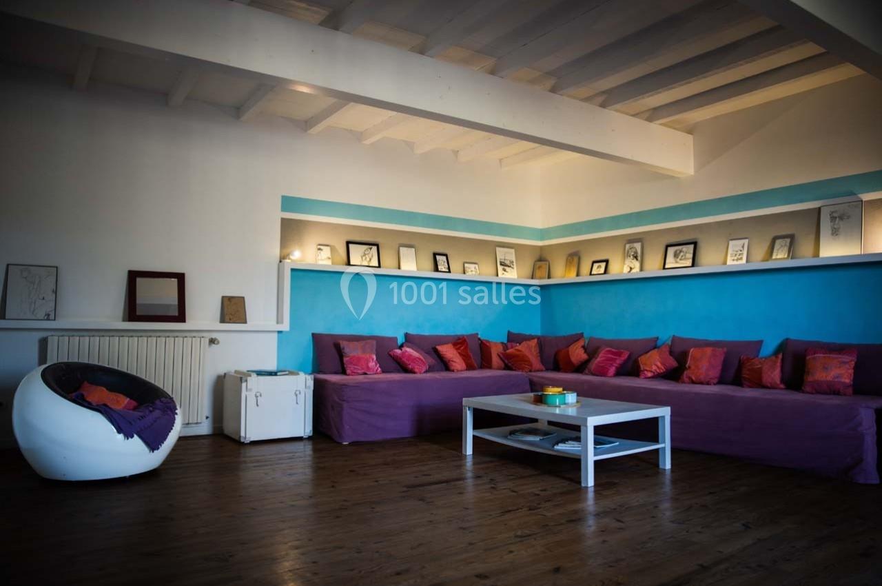 Salon avec un canapé d'angle violet, coussins colorés, table basse blanche et étagères décorées de cadres.