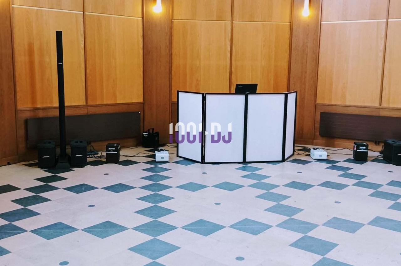 Configuration d’un espace DJ avec une table blanche, des enceintes et des lumières dans une salle au sol carrelé.