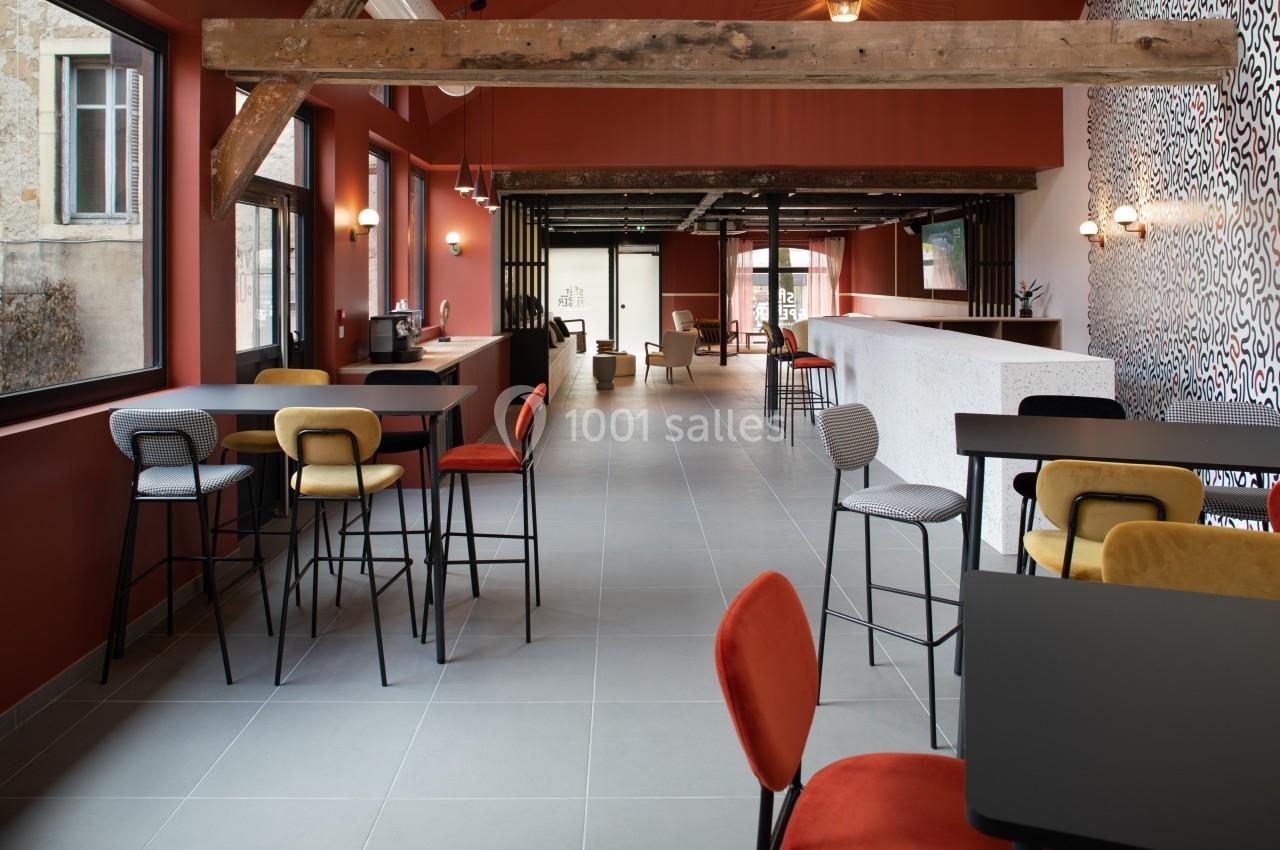 Salle lumineuse avec poutres apparentes, mobilier coloré et comptoir blanc, aménagée pour des espaces de travail ou détente.