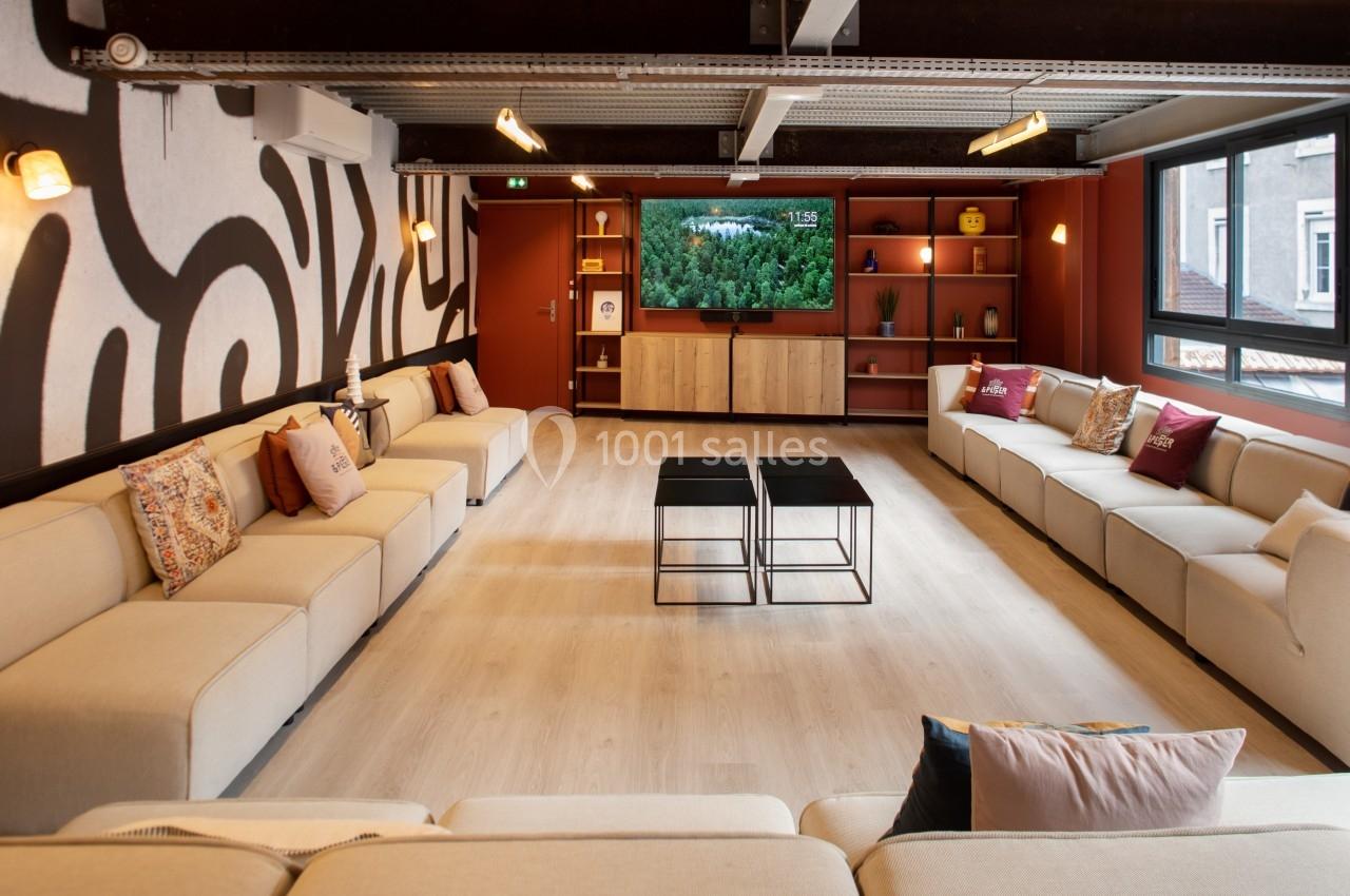 Salle de séjour spacieuse avec canapés beiges, tables basses noires, étagères décorées et télévision allumée.