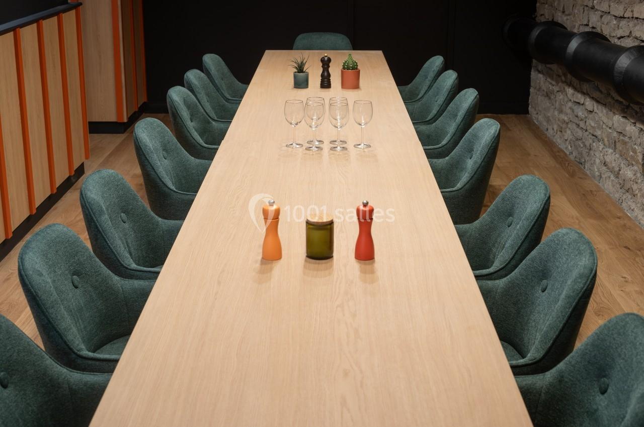 Grande table en bois entourée de chaises vertes, avec des verres, des plantes et des accessoires de table au centre.