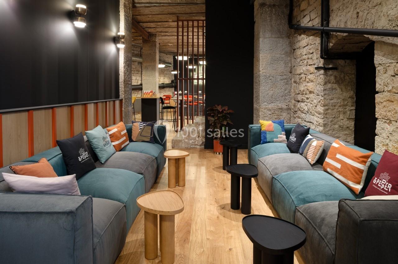 Espace salon avec canapés colorés, coussins variés, tables basses en bois et murs en pierre dans un cadre chaleureux.