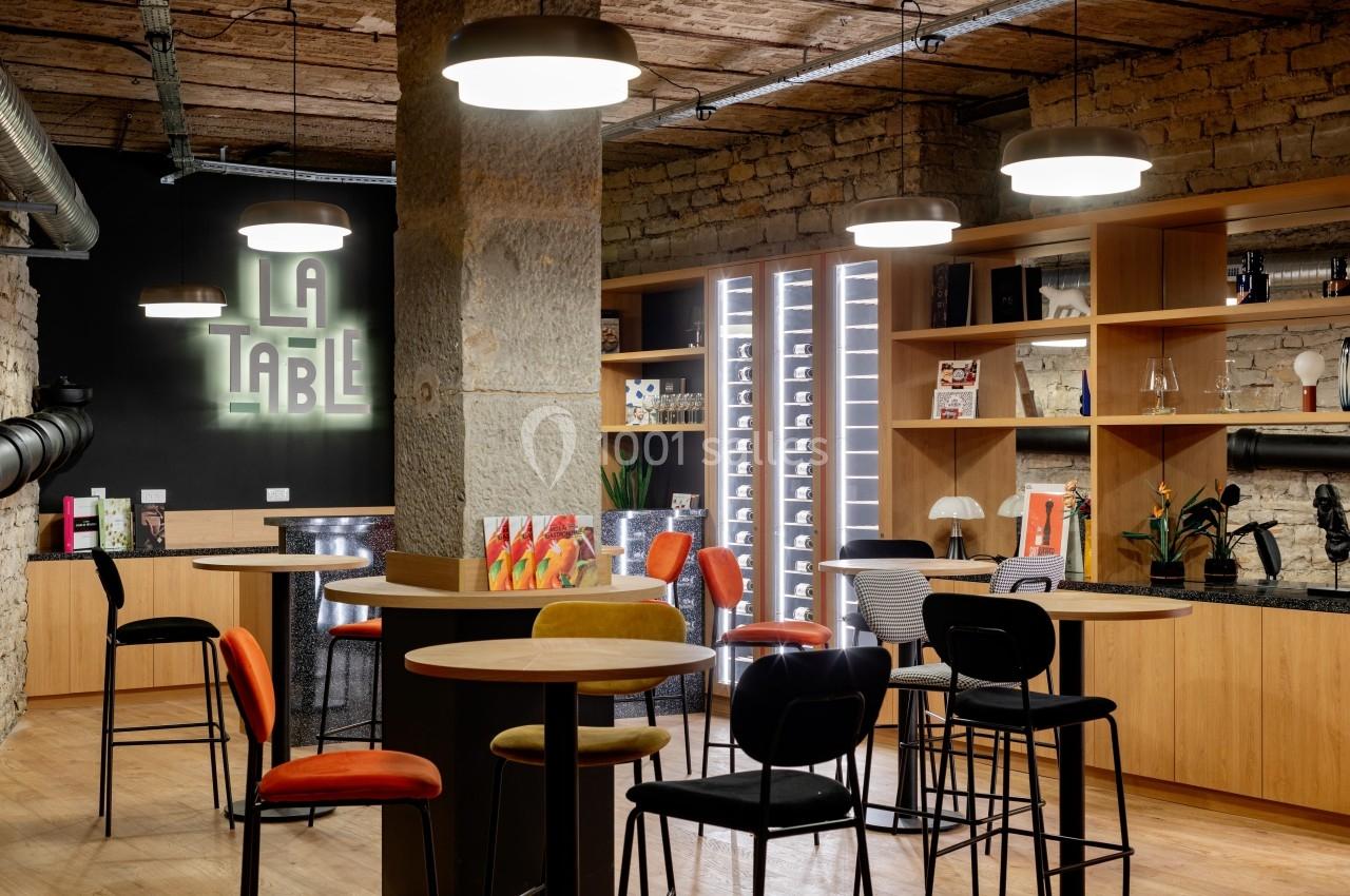 Espace intérieur moderne avec tables hautes, chaises colorées, étagères décorées et enseigne lumineuse ’La Table’.