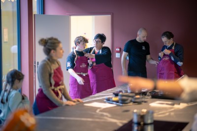 Deux femmes en tablier rouge discutent en préparant des ingrédients dans une cuisine moderne.