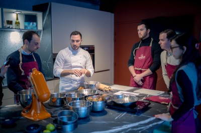 Deux femmes en tablier rouge discutent en préparant des ingrédients dans une cuisine moderne.