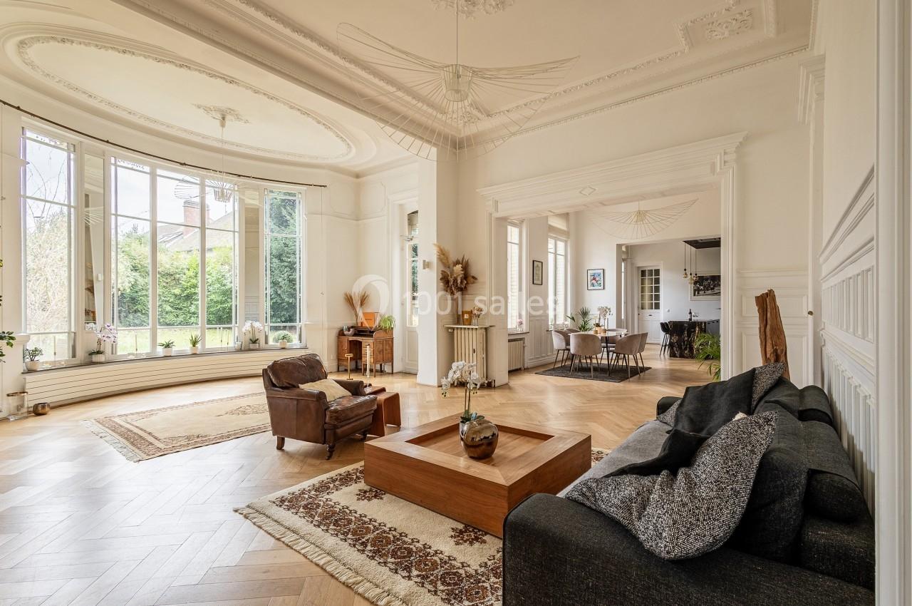 Salon lumineux avec parquet en bois, grandes fenêtres, mobilier moderne et vue sur un jardin extérieur.