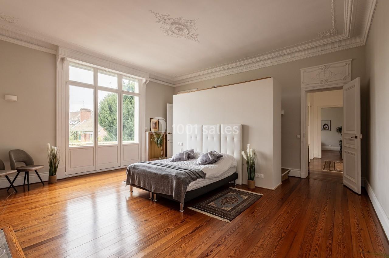 Chambre lumineuse avec parquet en bois, lit double, moulures au plafond et grande fenêtre donnant sur un jardin.