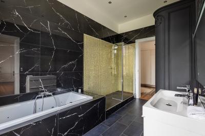 Salle de bain avec baignoire encastrée, douche à l'italienne, carrelage noir marbré et mosaïque dorée.