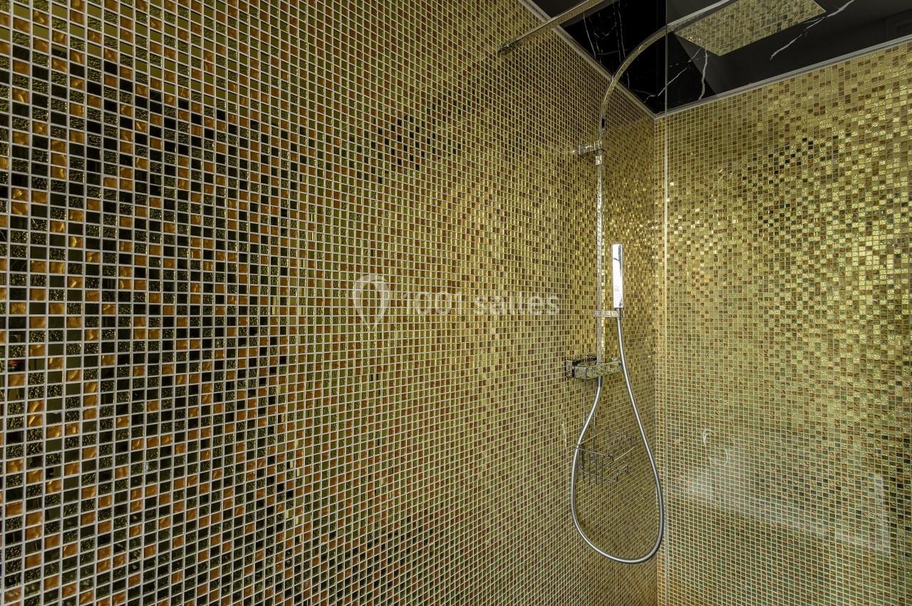 Douche moderne avec carrelage en mosaïque dorée et pommeau de douche mural.