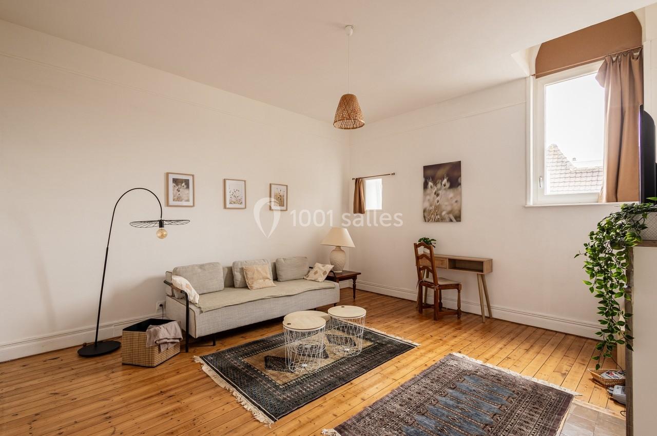 Salon lumineux avec parquet, canapé gris, tapis, bureau en bois, et décoration murale minimaliste.