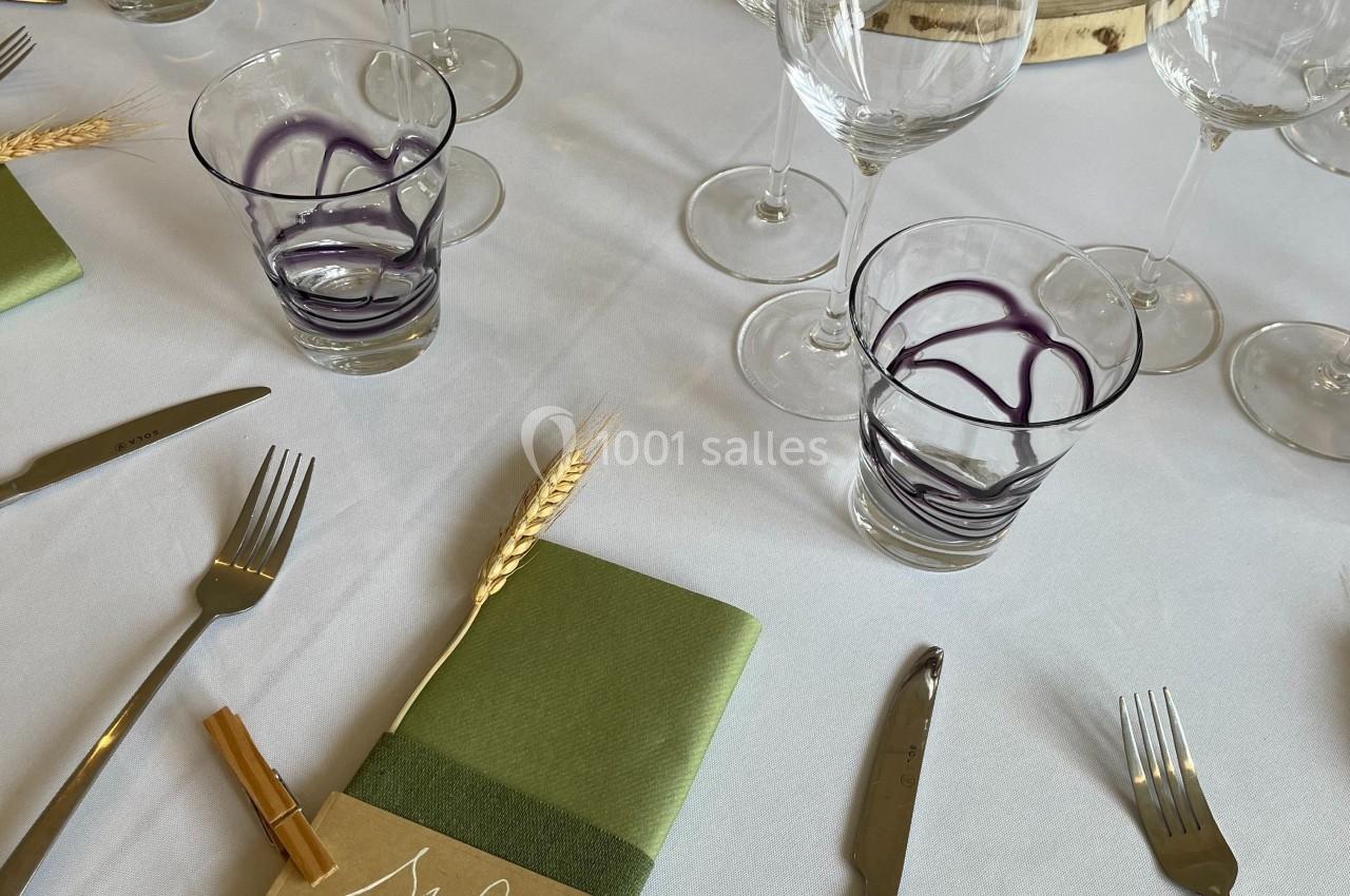 Table dressée avec des verres, couverts, serviettes vertes et marque-places personnalisés sur une nappe blanche.