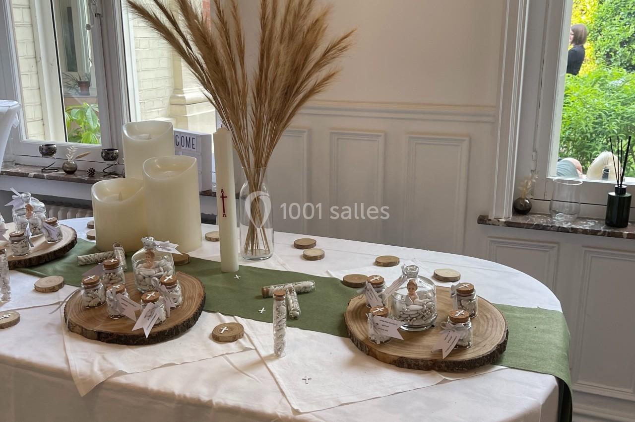 Table décorée avec des bougies, des herbes séchées et des petits pots en verre sur des rondins de bois, près d'une fenêtre.
