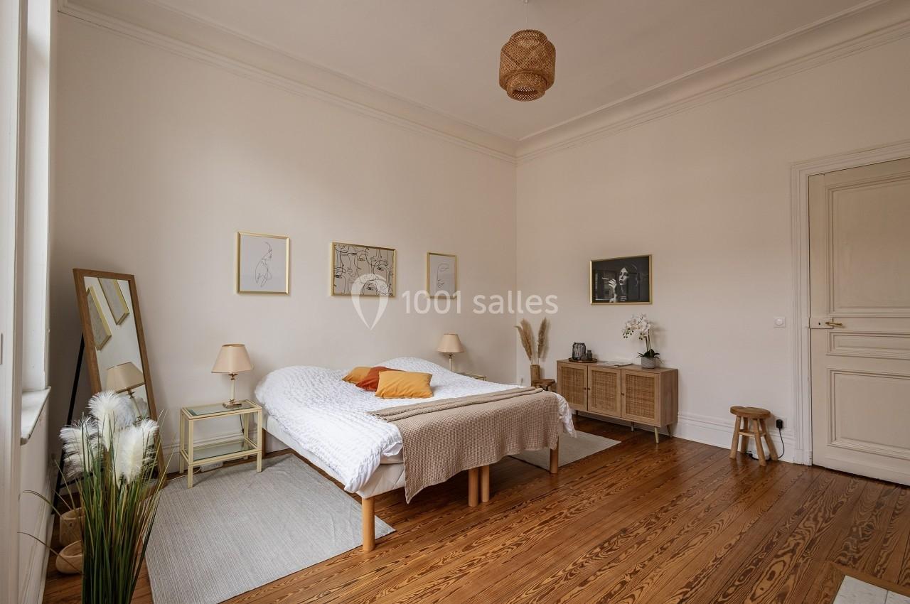 Chambre lumineuse avec lit double, parquet en bois, miroir, meubles en rotin et décorations murales minimalistes.
