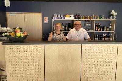 Un homme et une femme souriants derrière un comptoir en bois, avec des étagères de boissons en arrière-plan.