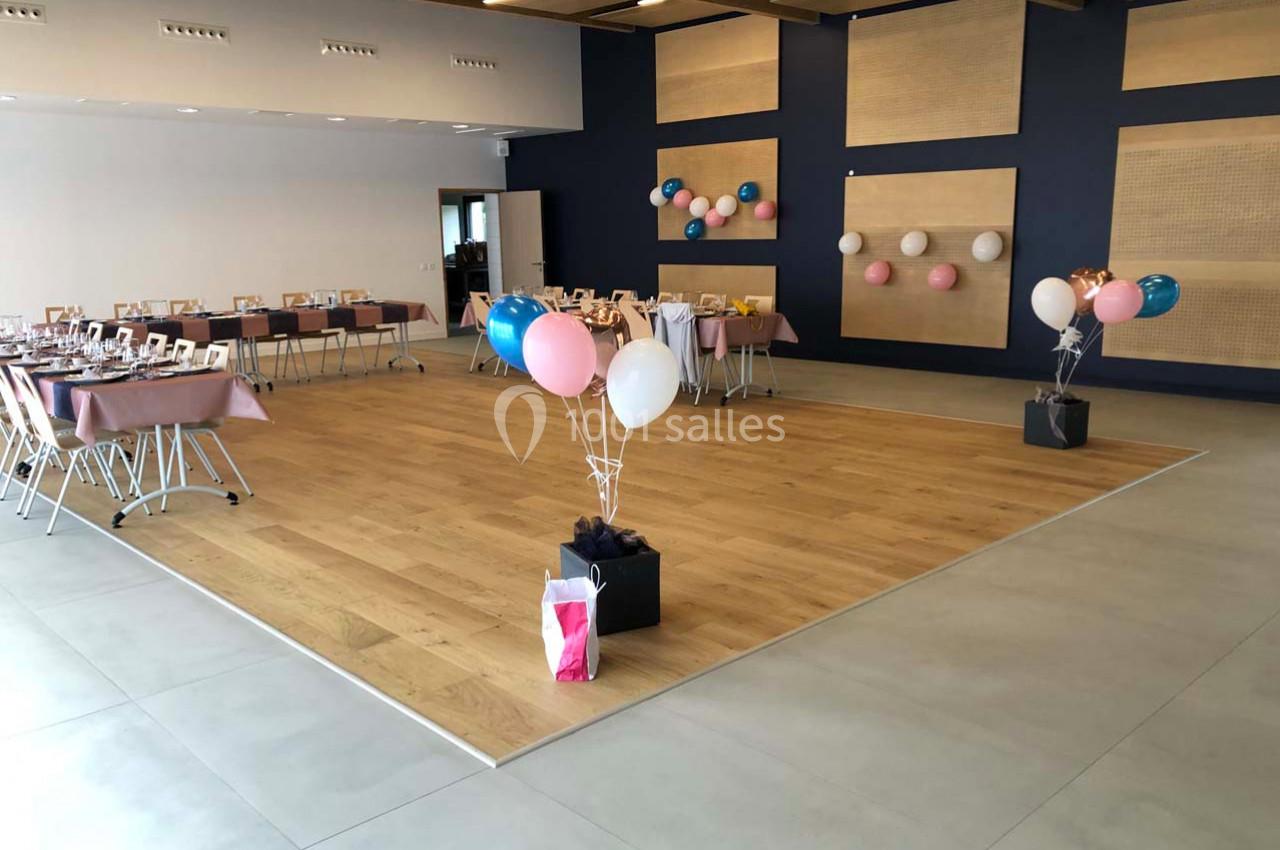 Salle décorée pour un événement, avec des tables dressées, des ballons colorés et un parquet central dégagé.