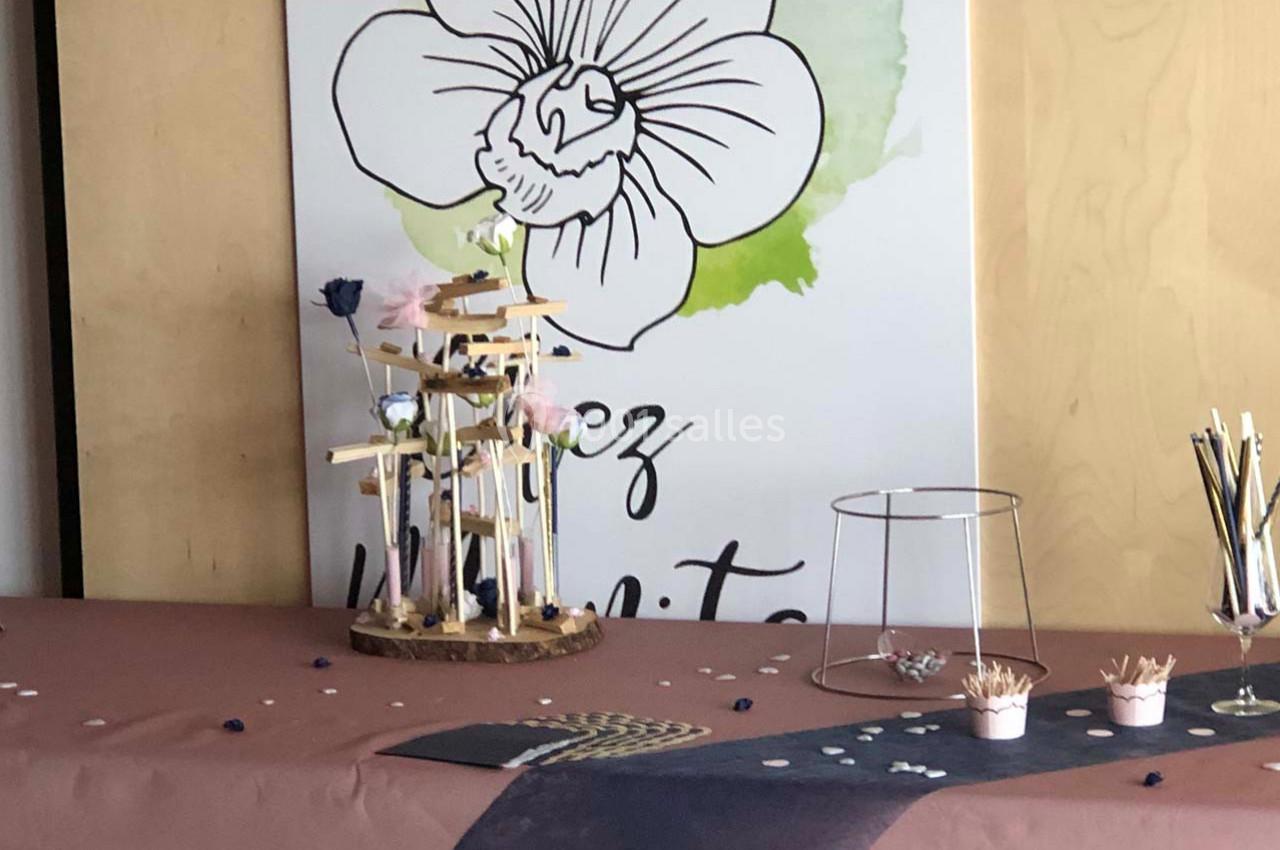 Décoration de table avec un présentoir en bois, des fleurs, des crayons et une affiche illustrée en arrière-plan.