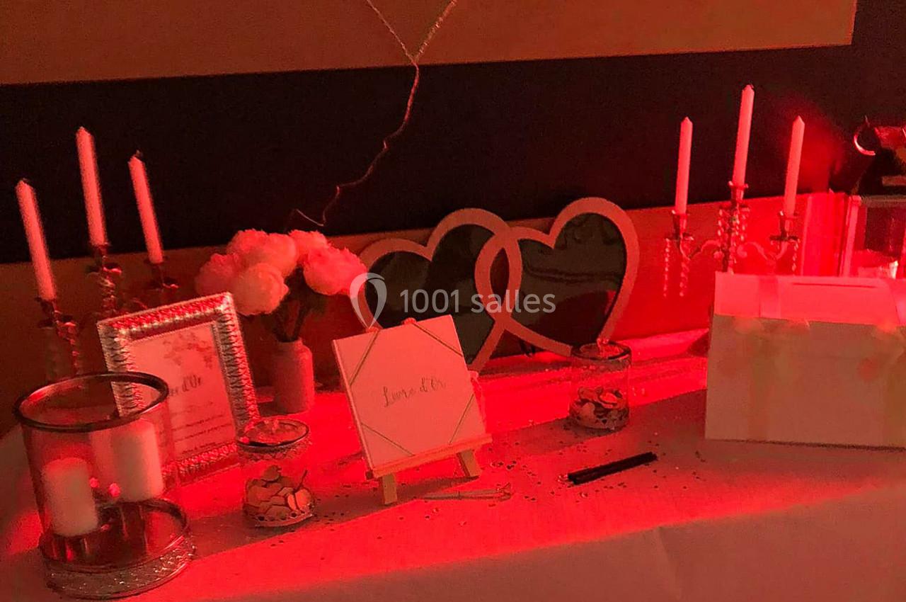 Table décorée avec des bougies, cadres, fleurs et une boîte blanche, éclairée par une lumière rouge tamisée.