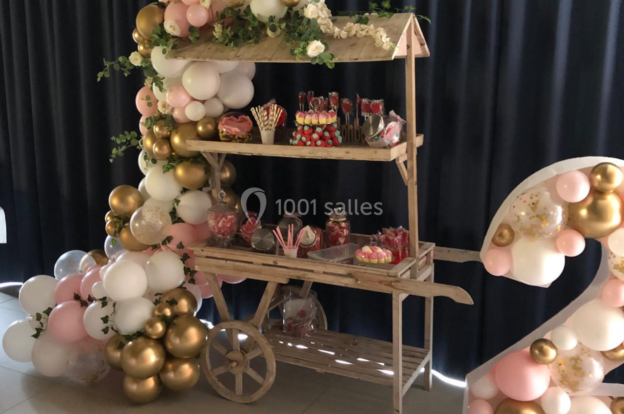 Chariot en bois décoré de ballons et de fleurs, présentant des bonbons et friandises dans un décor festif.