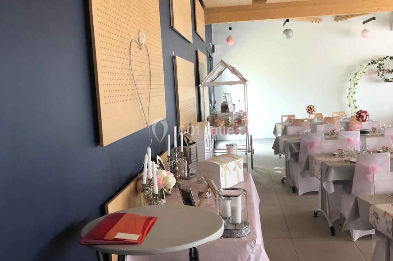 Salle décorée pour un événement avec tables habillées de nappes roses, décorations florales et coin buffet.