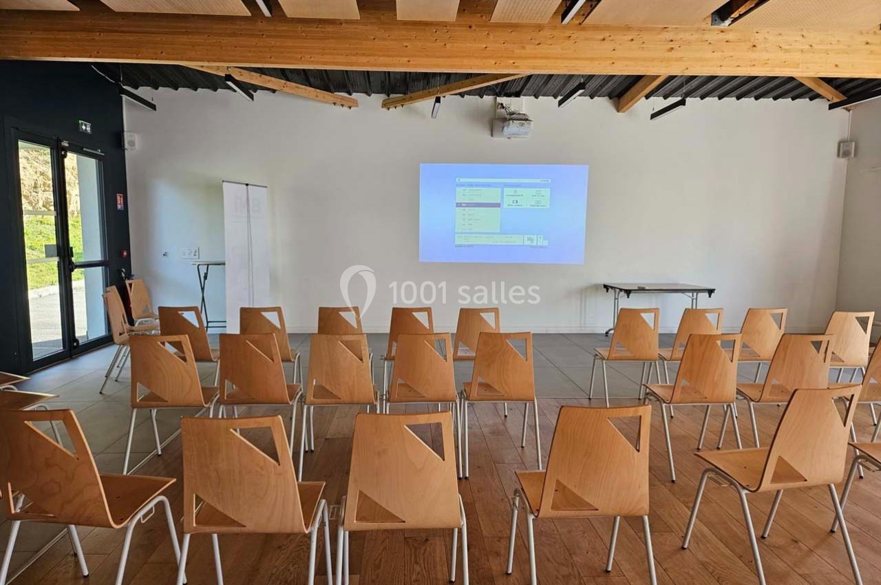 Salle de réunion avec des chaises en bois alignées face à un écran de projection affichant une présentation.
