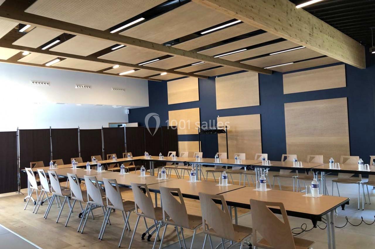 Salle de réunion lumineuse avec tables disposées en U, chaises en bois clair et bouteilles d'eau alignées.