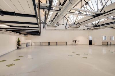 Salle lumineuse avec rangées de chaises, tables hautes et buffet en arrière-plan, sous un plafond industriel.