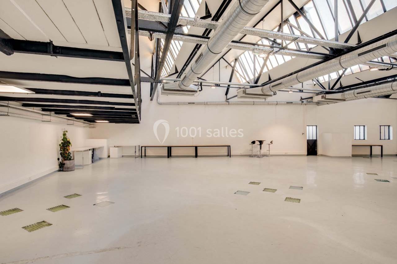 Intérieur d'un espace ouvert lumineux avec sol clair, plafond industriel et grandes fenêtres en verrière.