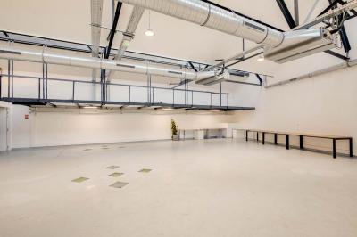 Salle lumineuse avec rangées de chaises, tables hautes et buffet en arrière-plan, sous un plafond industriel.