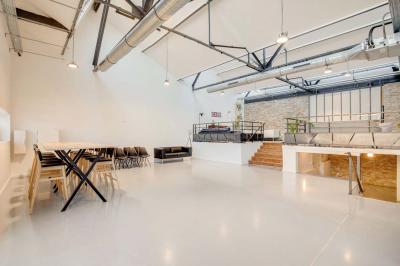 Salle lumineuse avec rangées de chaises, tables hautes et buffet en arrière-plan, sous un plafond industriel.