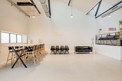 Salle lumineuse avec rangées de chaises, tables hautes et buffet en arrière-plan, sous un plafond industriel.